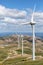 View of a wind turbines on top of mountains, dirt road and wild nature and landscape, cloudy sky as background