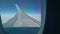 View of wing upper surface and wing tip framed by window of flying aircraft. Travelling by plane. Blue sky at background