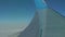 View of wing upper surface and wing tip through plane window of flying aircraft. Travelling by plane. Blue sky at