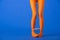 View of woman in bright orange tights holding fork and sausage with legs on blue