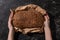 View of woman holding fresh baked loaf of whole grain bread in paper on stone black surface