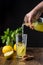 View of woman`s hand serving lemon juice in a glass on a table with lemons, mint, brown sugar and black