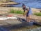 View of woman washing manioc in river waters to make manioc flour, rocks and herbs on the banks