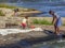 View of woman washing manioc in river waters to make manioc flour, rocks and herbs and children playing on the banks
