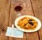 View of wooden table, plate of paella and glass of red wine, with protection mask with antibacterial gel, new normal in restaurant