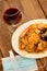 View of wooden table, plate of paella and glass of red wine, with protection mask with antibacterial gel, new normal in restaurant