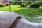 View at wooden terrace, stone path and green garden with hail stones during hailstorm from sky with sunlight