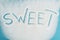 View of word sweet made on sprinkled white sugar crystals on blue surface