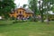 View of a yellow village house with swedish flag on the roof. Many guests coming for outdoor party on a summer day.