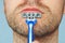 View of a young bearded man with a brutal razor. face on the blue background. big rough hairy bristles on the skin, close up