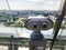 Viewing coin stationary binoculars against a white-blue sky in profile. Gray metal binoculars on the viewing platform at a height.