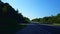 Viewpoint of multiple vehicles on rural street from side of road in summer. Roadside view of transportation traffic approaching