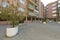 Views of brick building facades and a public square with circular cement planters and young trees inside