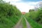 Village dirt road meanders among the hills, houses with a red roof in the background, summer village landscape, green field with