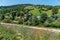 The village street with neat houses is located at the foot of the hill with green slopes and the current below the river