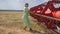 Villager female into dress dances in slow motion at field on background agricultural machinery