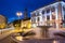 Vilnius Lithuania. Gray Marble Fountain, Water Jets On Illuminated Rotuses Square, Summer Blue Sky