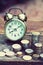 Vintage alarm clock and coin pile on wooden table with blur green garden background, bright morning color tone, finance and