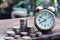 Vintage alarm clock and coin stacks on wooden table with blur green garden background, bright morning color tone, finance and