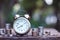 Vintage alarm clock and coin stacks on wooden table with blur green garden background, bright morning color tone, finance and