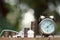 Vintage alarm clock and coin stacks on wooden table with blur green garden background, bright morning color tone, finance and