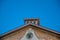 Vintage back face clock with gold Roman numerals on an old brick building with blue sky background.