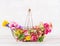 Vintage basket with various colorful garden flowers at white wooden background, front view. Summer gardening