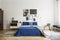 Vintage bedroom interior with bedside table, king size bed with blue bedding and pillows. Mockup gallery on the white wall