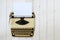 Vintage beige typewriter from the 1950s with paper on a white painted wooden background, copy space, high angle view from above