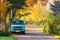 Vintage camping car on road with colorful autumn foliage trees.