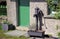 Vintage cast iron water pump outside a house with green door and window frames, in a rural rustic setting on a sunny day