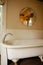 Vintage clawfoot cast iron bathtub in white and creme bathroom with wall decor and round mirror