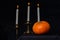 Vintage copper candlestick with three burning white candles and a whole orange pumpkin on a black background, close-up
