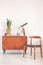 Vintage cupboard with plant, books, telescope and clock next to stylish wooden chair in white and bright interior with copy space