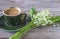 Vintage green cup of coffee and bouquet of lilies of the valley on the old non paint wooden background.