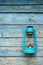 Vintage handle gas lantern on rustic wooden wall. Old fashioned dusty kerosene oil lamp in blue color. Camping light. Interior