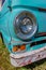 Vintage headlight on an old, abandoned blue van with a rusty bumper