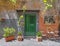 Vintage house exterior with green entrance door on ocher wall and flower pots.