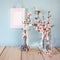 Vintage jewelery stand with pearls necklace, blank frame next to white spring flowers on wooden table