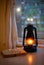 Vintage kerosene lamp with fire on a blurred background of the window and curtains with a book and glasses