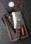 Vintage meat knife and fork and hatchet in old wooden box on black table background. Butcher utensils. Salt and pepper