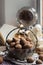 A vintage metal and glass vase with walnuts, in the background an antique clock, a marble figurine of a bear and an open book.