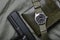 Vintage military watch with nato strap and pistol on army green background, Classic timepiece mechanical wristwatch