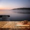 Vintage notebook and stack of wooden colorful pencils on wooden texture table in front of calm foggy lake view at sunset