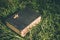 Vintage old holy bible book, grunge textured cover with wooden christian cross. Retro styled image on grass background.