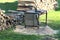 Vintage old metal circular saw table with rubber gloves next to stacked firewood ready for sawing surrounded with pile of saw dust