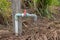 Vintage Old PVC Water Faucet with Red Plastic Valve - Abandoned Garden with Green Plants and Dry Grass