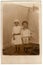 Vintage photo shows siblings - girl and boy pose in the backyard. Boy wears a sailor costume and girl wears a white