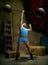 Vintage portrait of retro circus strongman wearing blue striped sports swimsuit training with barbell over dark circus