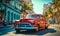 Vintage red classic car cruising on a sunny street in Havana with historical architecture and tropical vibes, capturing the